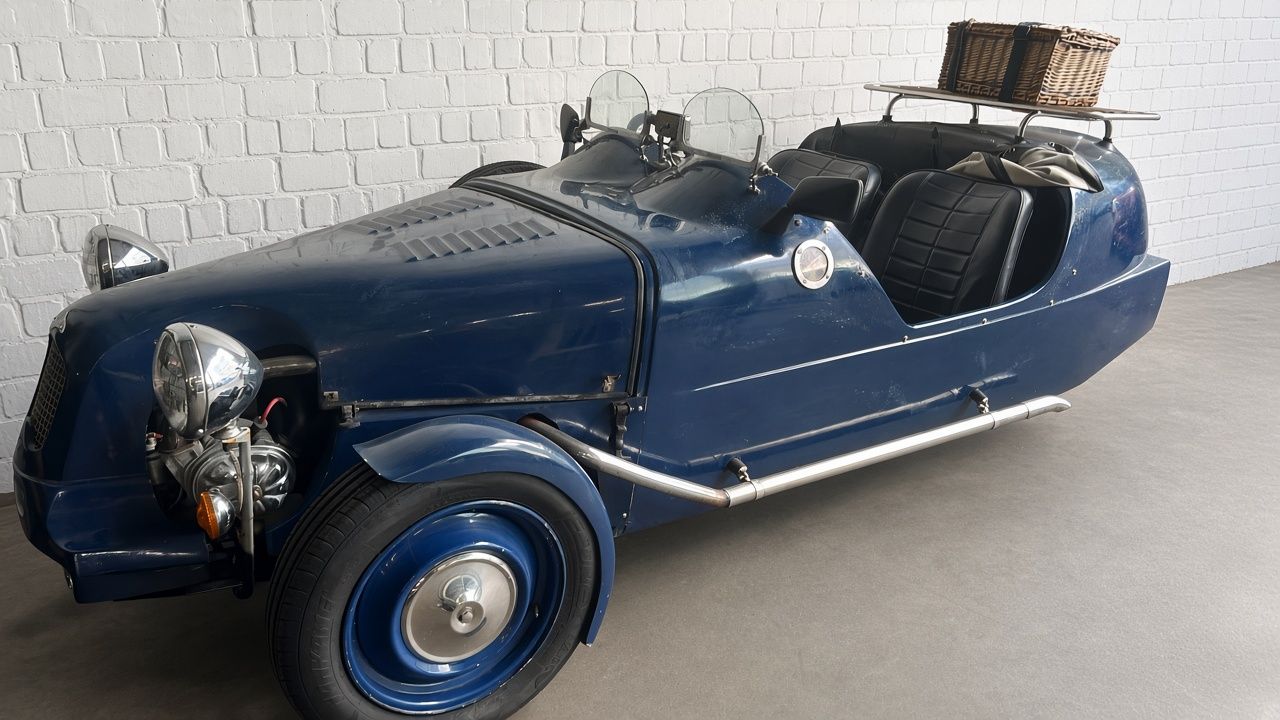 Blauwe driewielige vintage roadster met lederen zetels en bagagerek met mand
